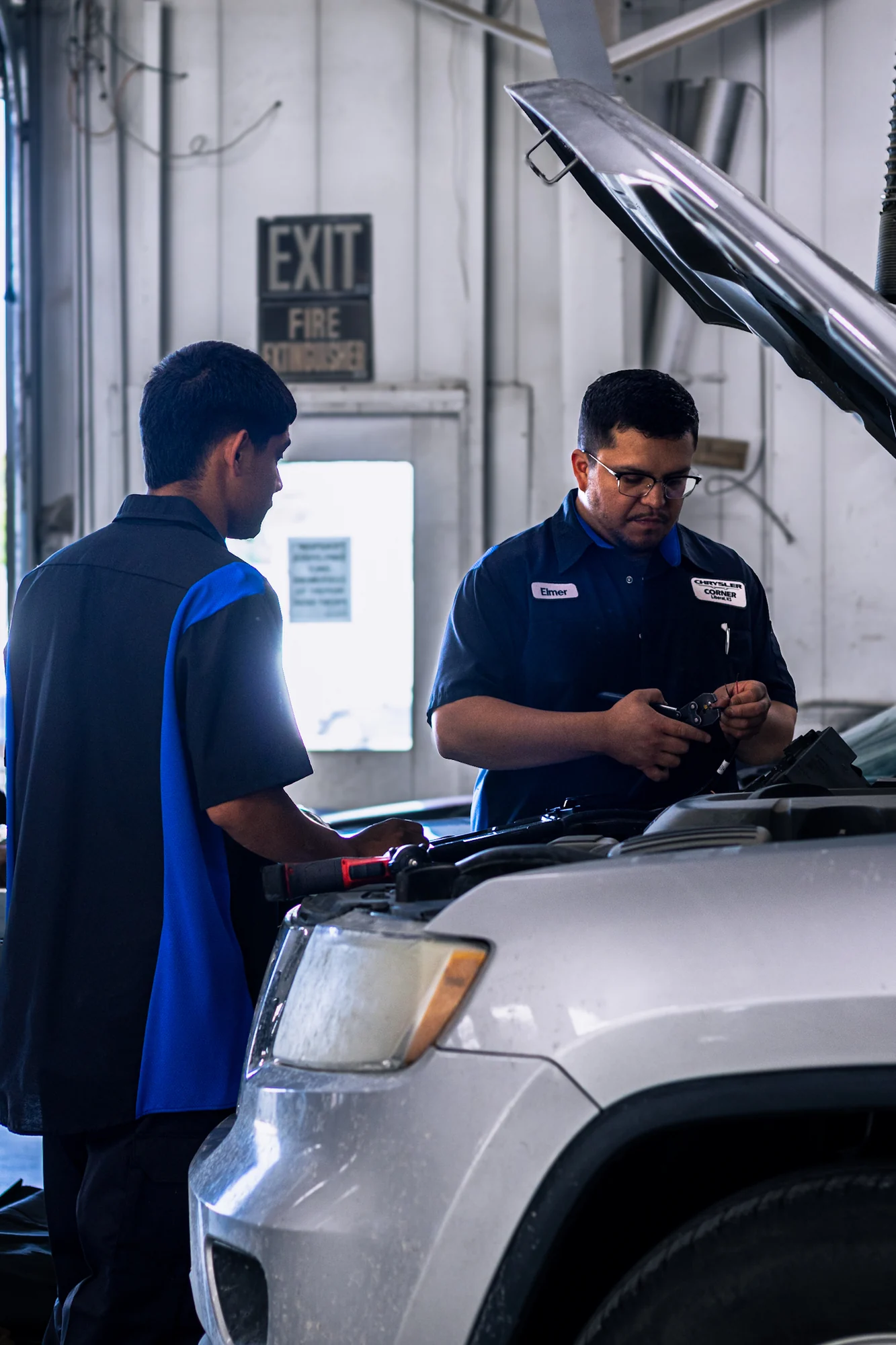Two Chrysler Corner technicians working under an open hood with a diagnostic tool