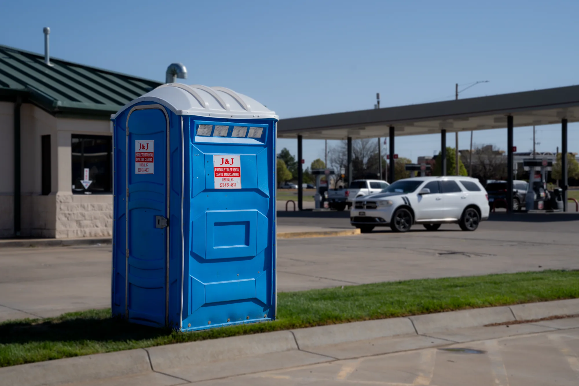 A branded J and J Services LLC portable toilet placed outside a commercial building
