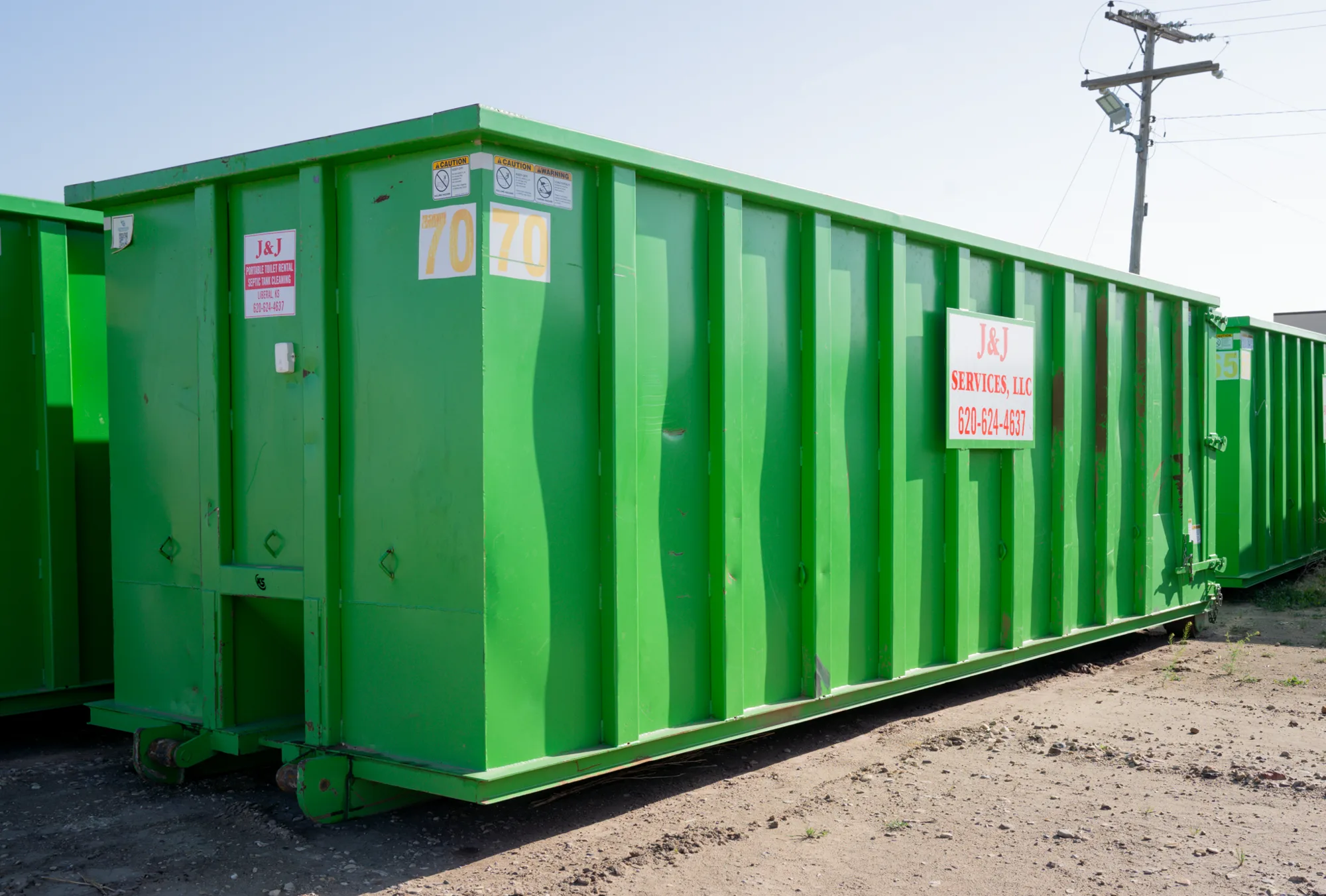 A green J and J Services LLC roll-off container staged in the yard