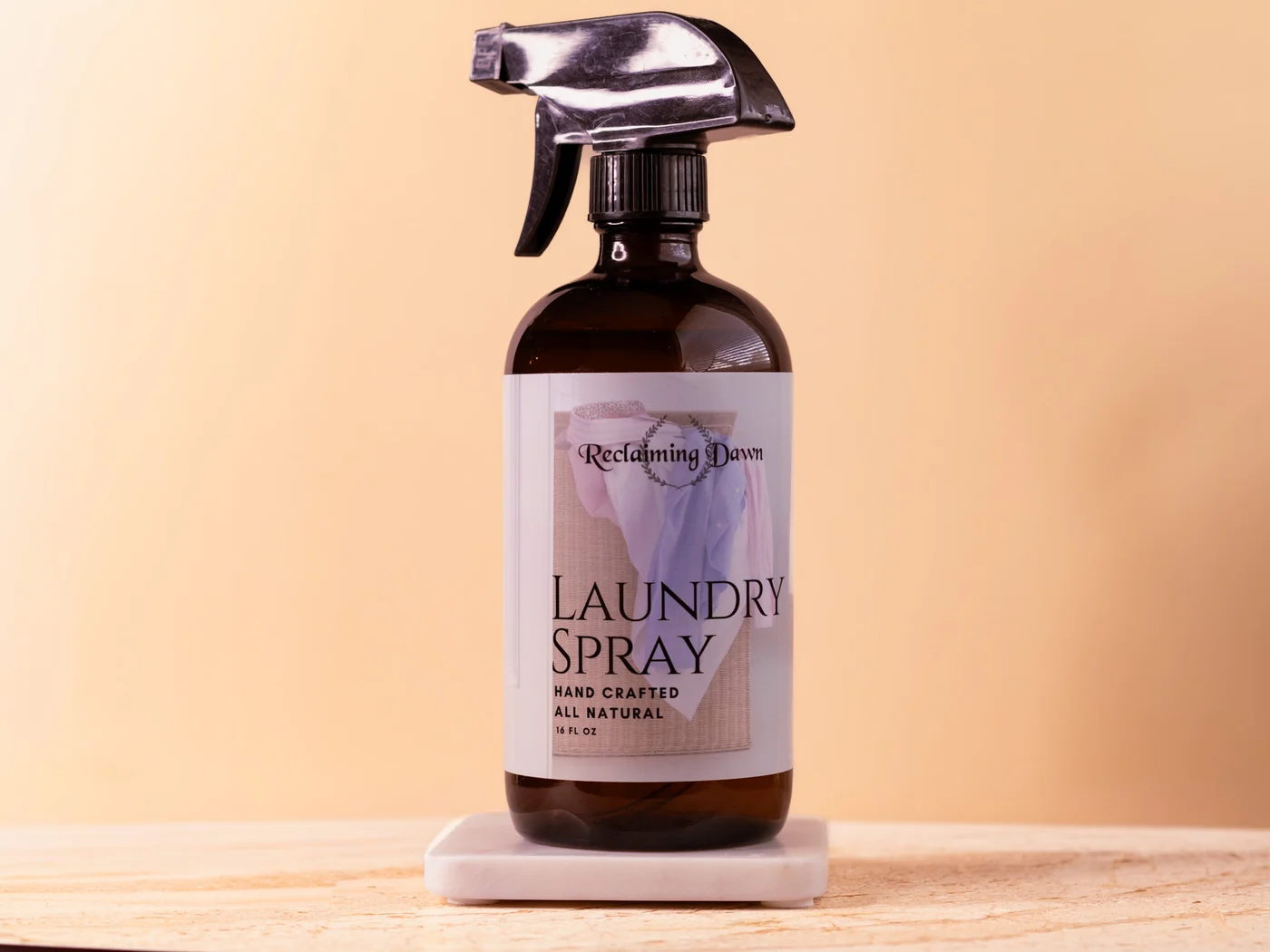Reclaiming Dawn laundry spray on a marble riser against a warm tan backdrop