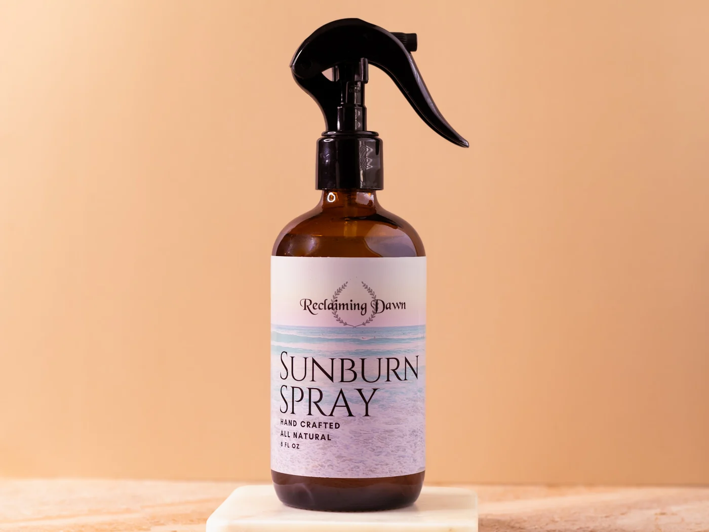 Reclaiming Dawn sunburn spray on a marble riser against a warm tan backdrop
