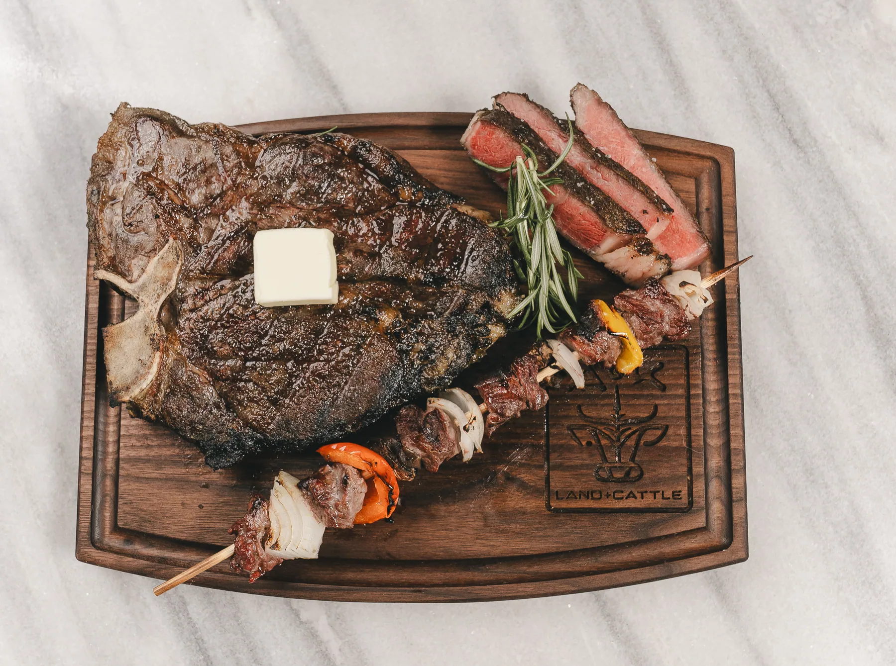 Grilled A&K Land and Cattle ribeye and beef skewers on a branded walnut board