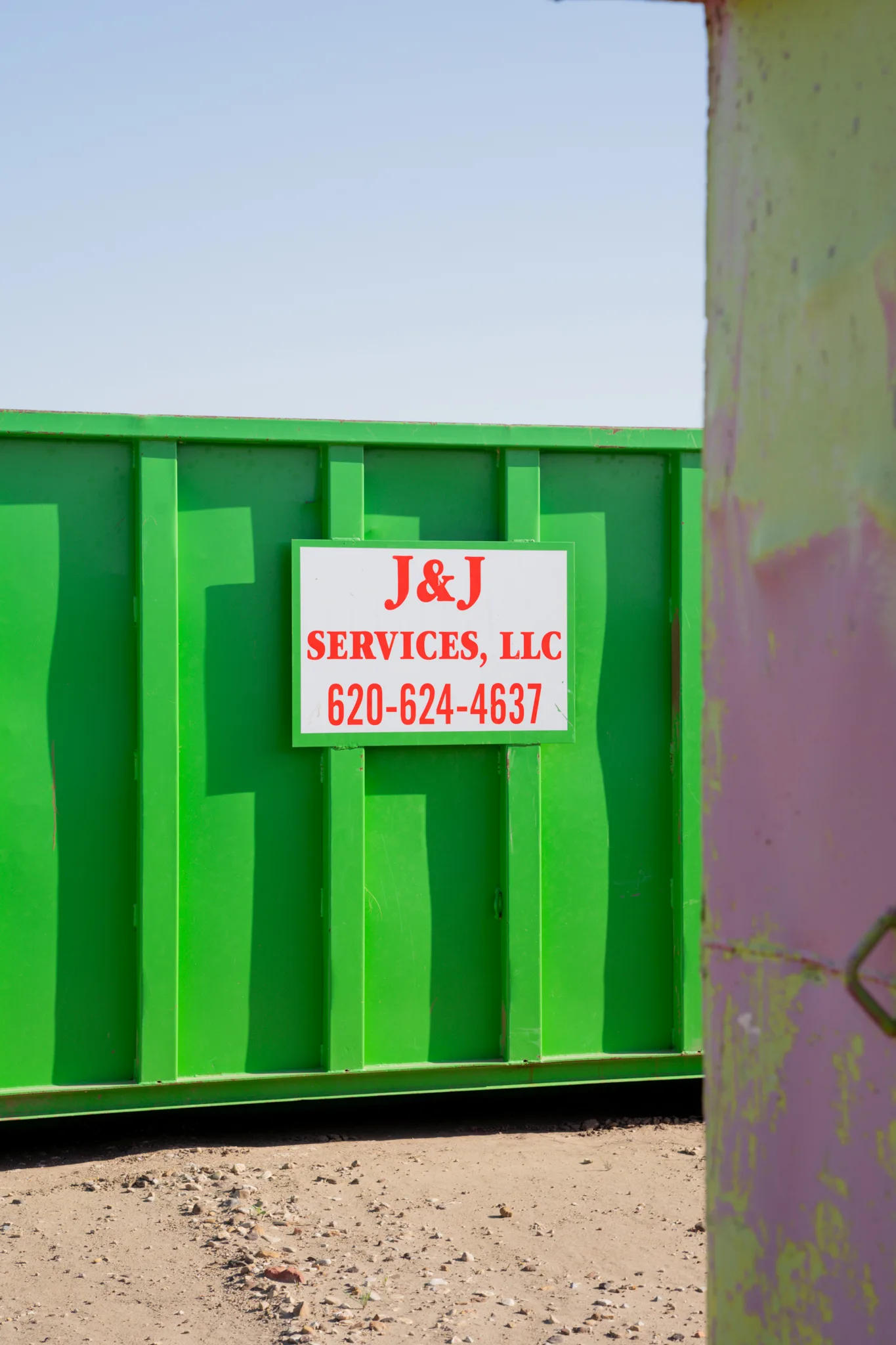 Close-up of the J and J Services LLC placard mounted on a green roll-off container