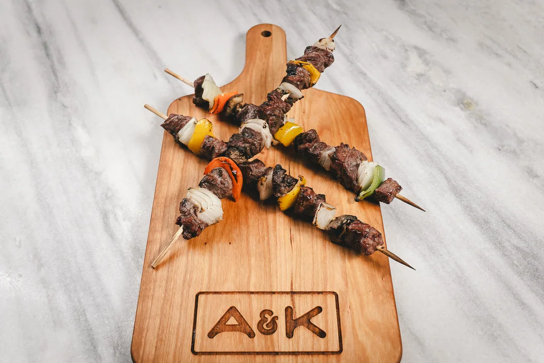 A&K beef skewers on a branded serving paddle