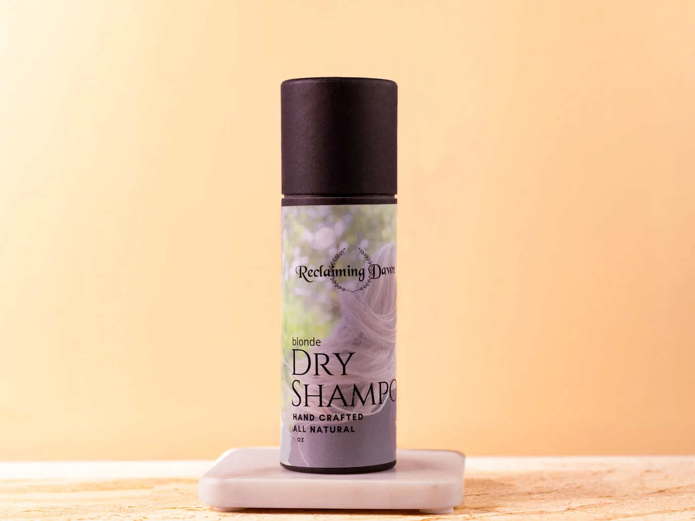 Reclaiming Dawn dry shampoo on a marble riser against a warm tan backdrop