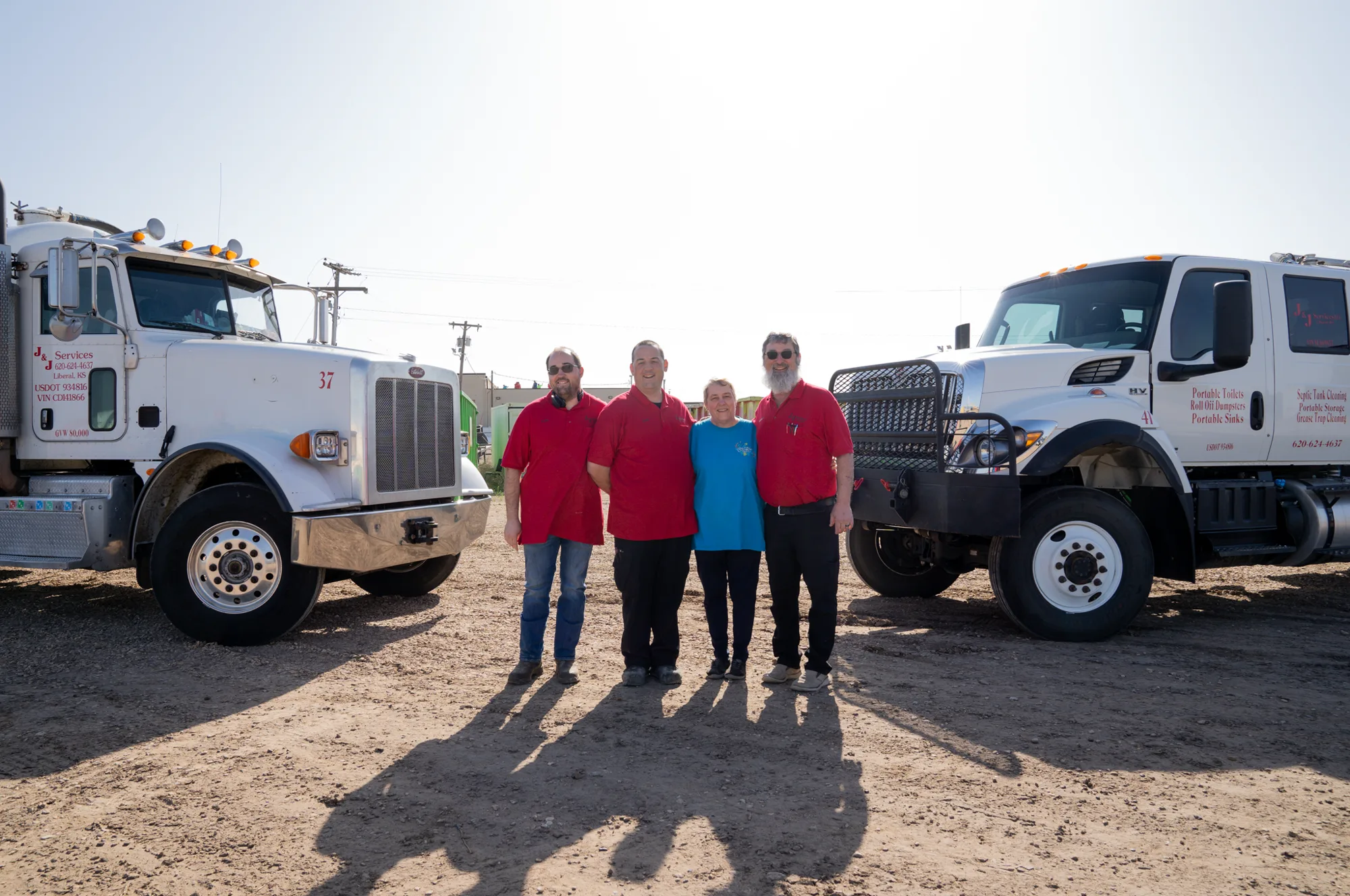 Four J and J Services LLC team members standing between two service trucks