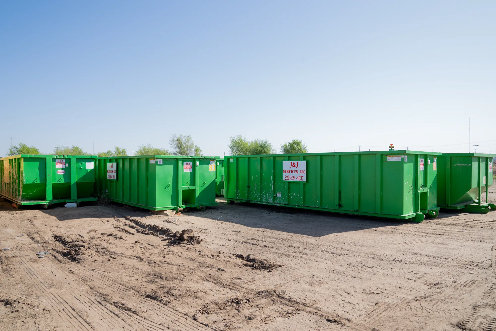 A long row of green J and J Services LLC roll-off containers in the yard