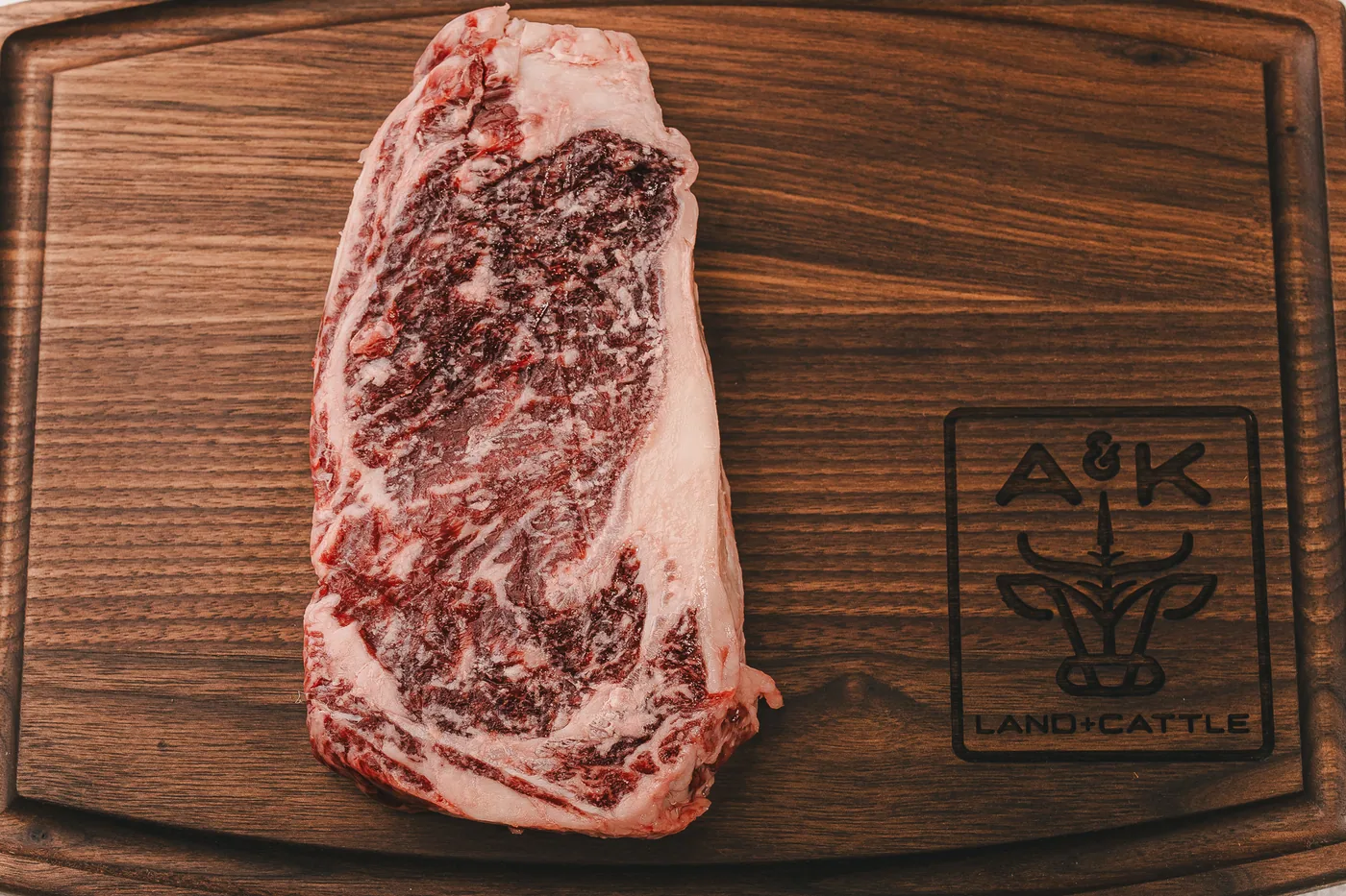 Raw A&K Land and Cattle ribeye on a branded walnut cutting board