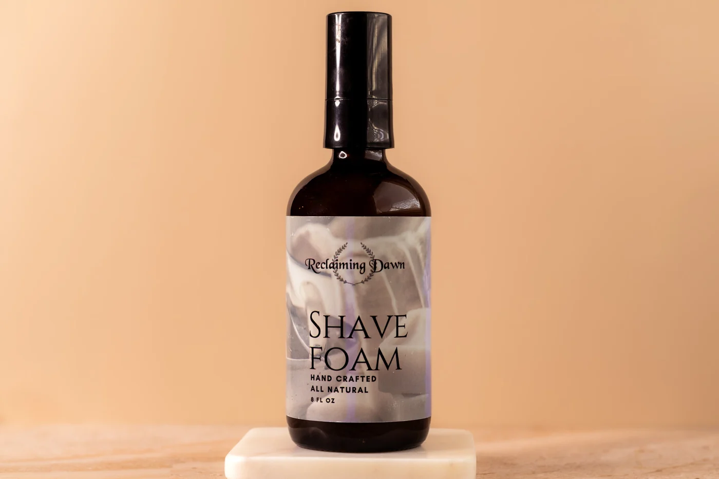 Reclaiming Dawn shave foam on a marble riser against a warm tan backdrop